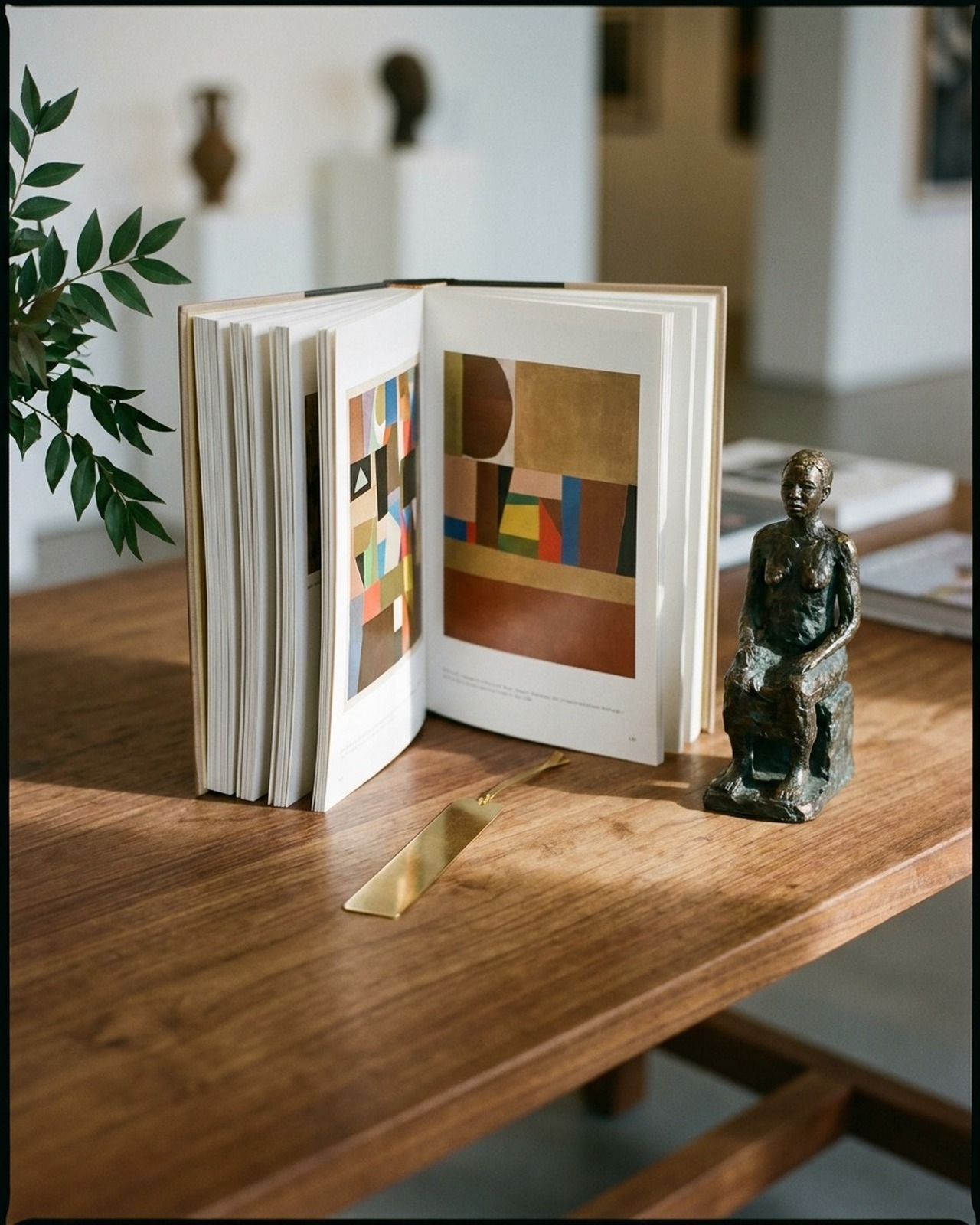 Contemporary Nigerian gallery interior, an open art monograph and bronze sculpture on a warm plaster reading table